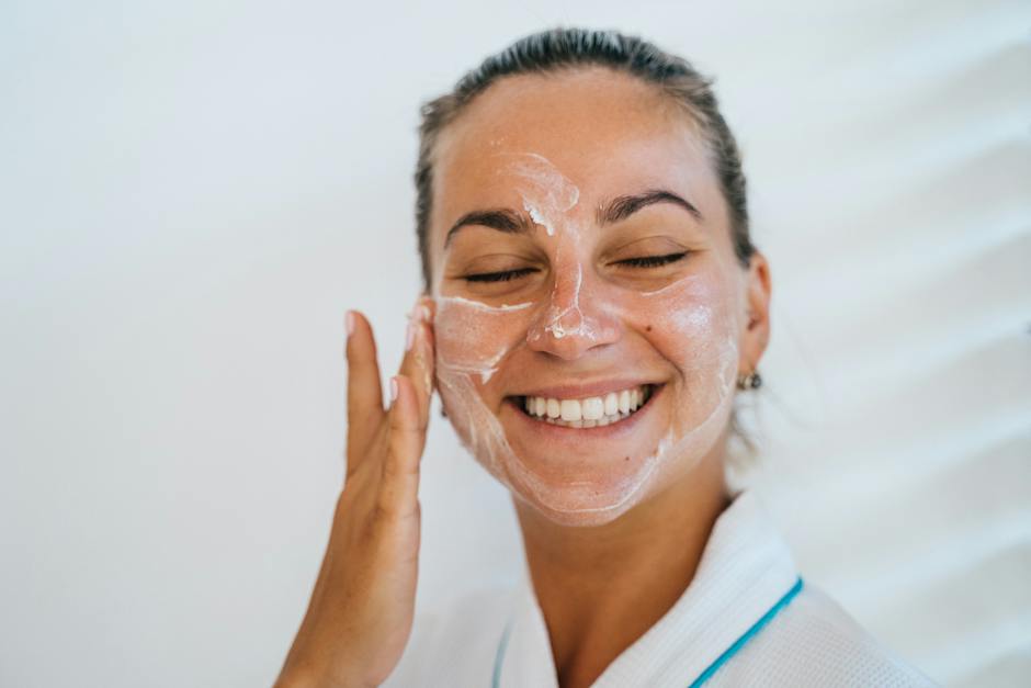 An image of a woman smiling and applying moisturizer to her face.